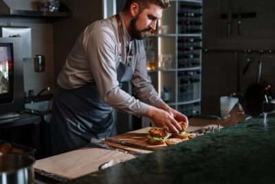 Chef preparing a gourmet beef burger with precision in a modern kitchen setting.